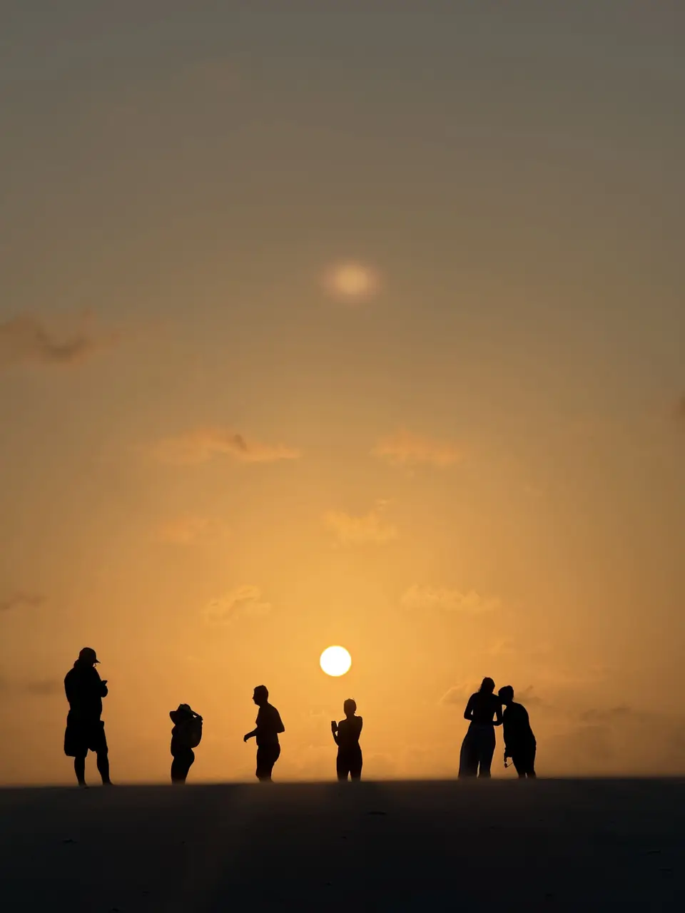 Grupo em silhueta contemplando o pôr do sol nas dunas dos Lençóis Maranhenses